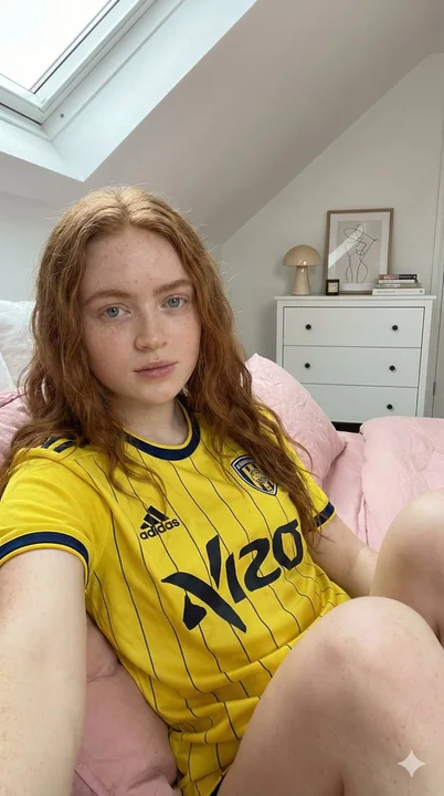 赤毛の少女が、黄藍のユニフォームを着て陽光に満ちたアトリエに立っている