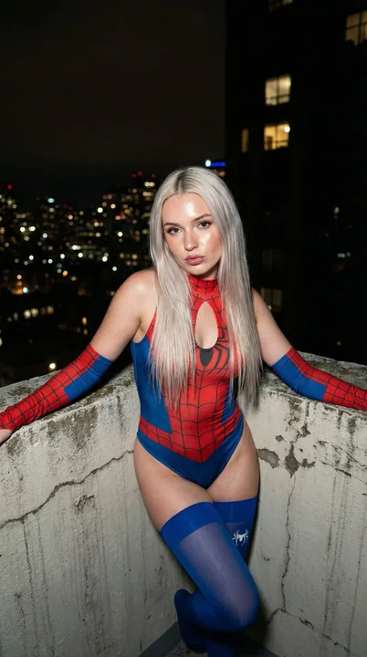 夜の幕がかかるビルの屋上に立つ金髪のスパイダーガール