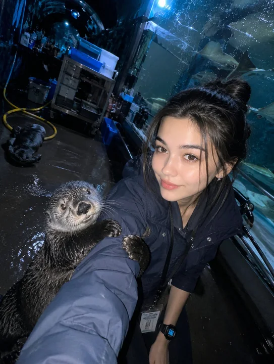 A keeper takes a selfie with a sea otter in a dim aquarium tunnel.