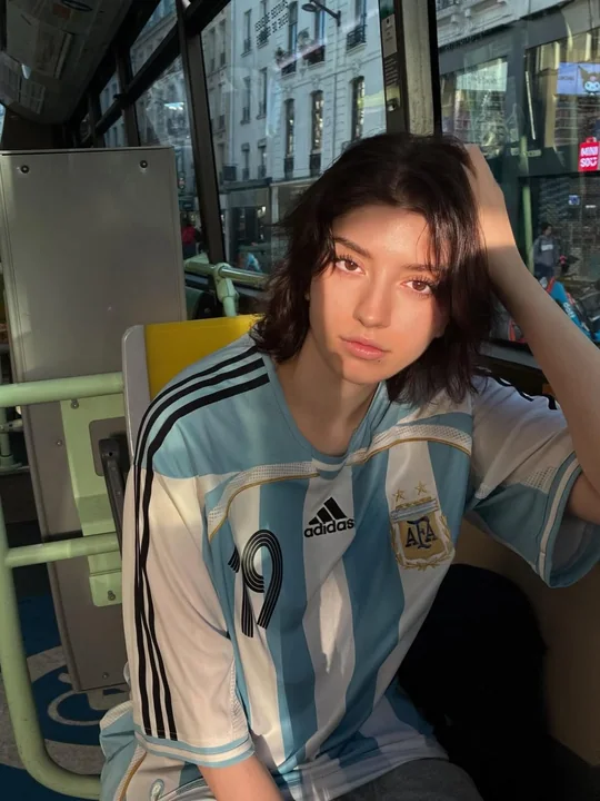 A realistic urban street-style portrait of a boy wearing an Argentina jersey.