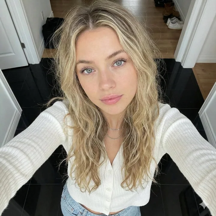 فتاة شقراء ترتدي قميصًا أبيض مصنوعًا من النايلون تأخذ selfie من زاوية مرتفعة بشكل جميل