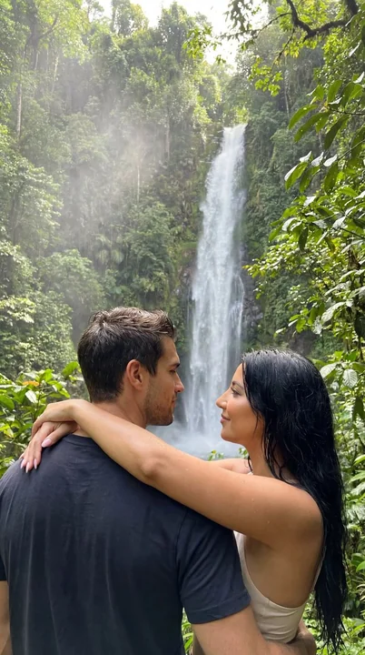 Ultra-realistic tropical rainforest couple embracing passionately amidst the mist of a waterfall