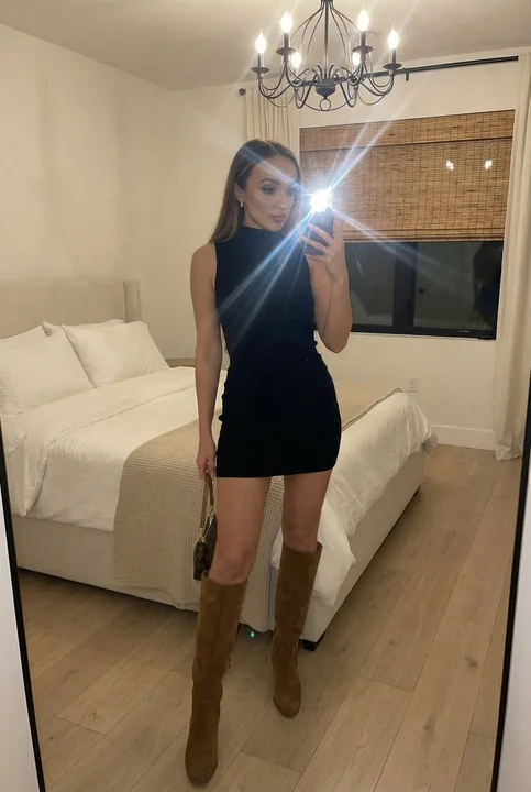 A fashionable internet influencer taking a full-body mirror selfie in a modern bedroom with flash.