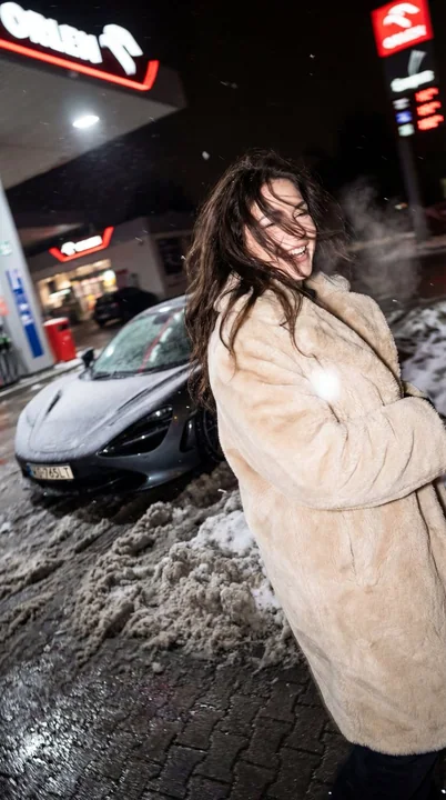 A slightly tipsy girl in fur beside a McLaren on a winter night