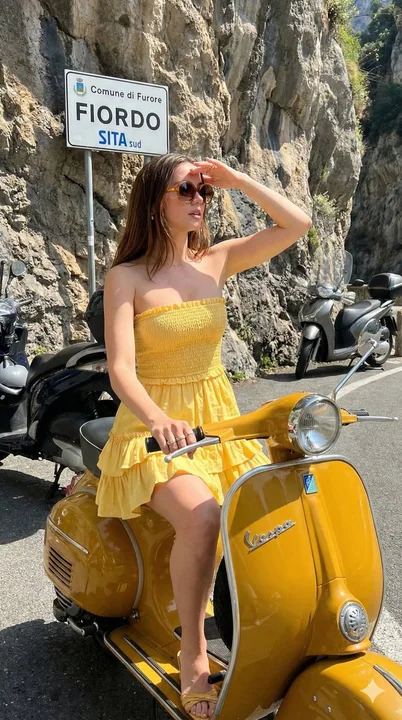 Jeune fille en robe jaune sous le soleil de la côte amalfitaine avec un scooter rétro